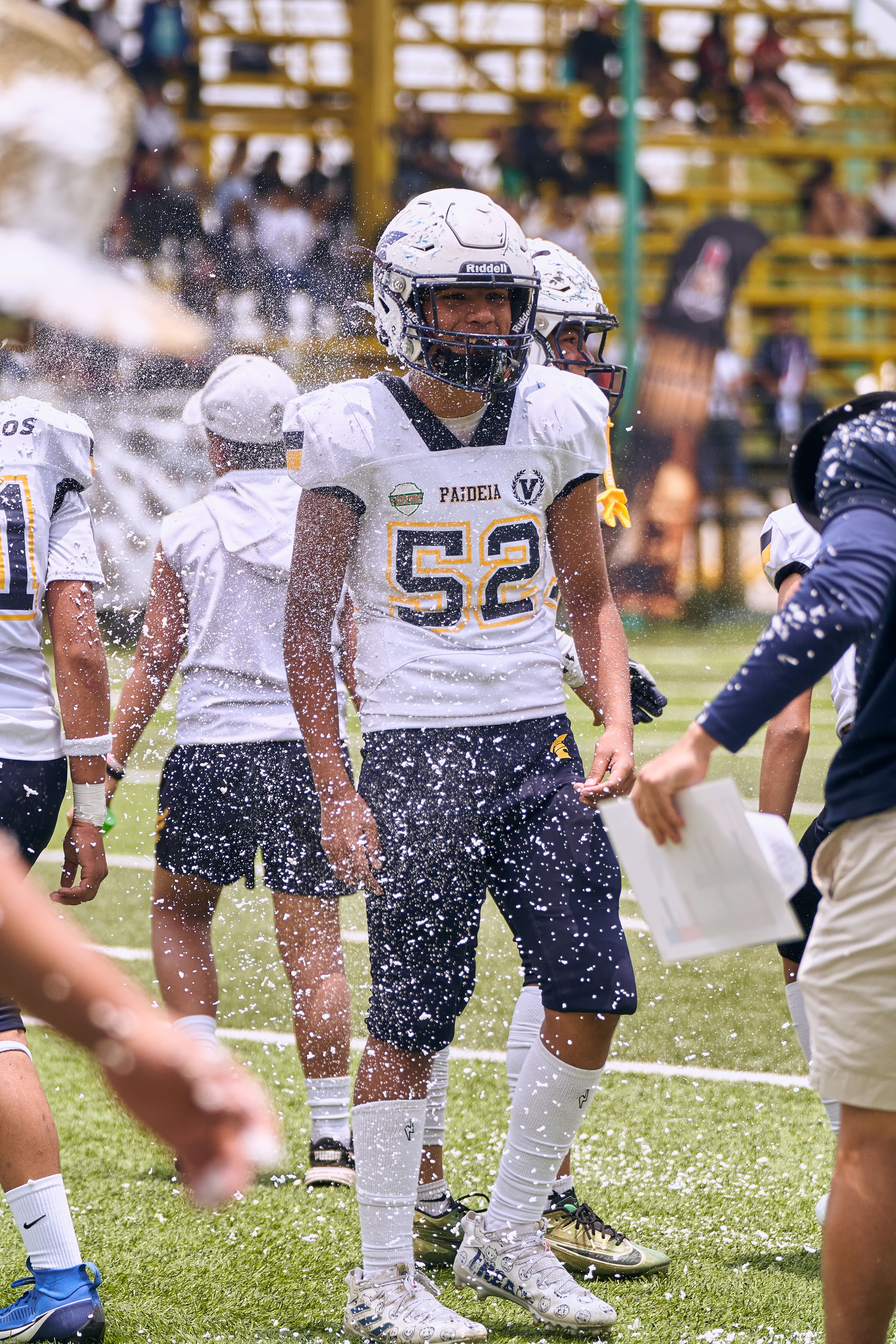 High school football players in uniform during a game with coach guidance and water splash.