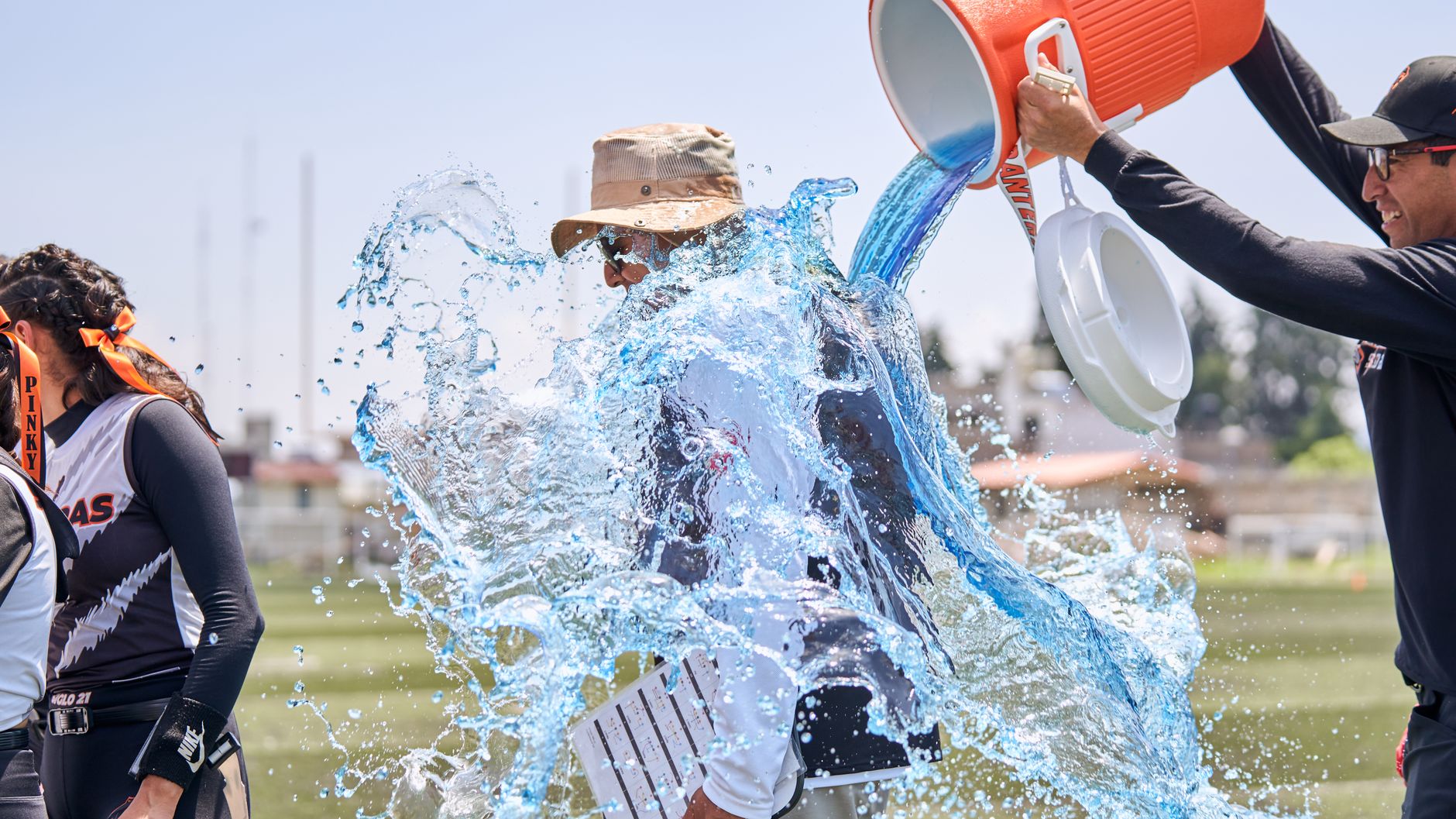 A joyous scene of a coach being doused with water during an outdoor sports celebration.