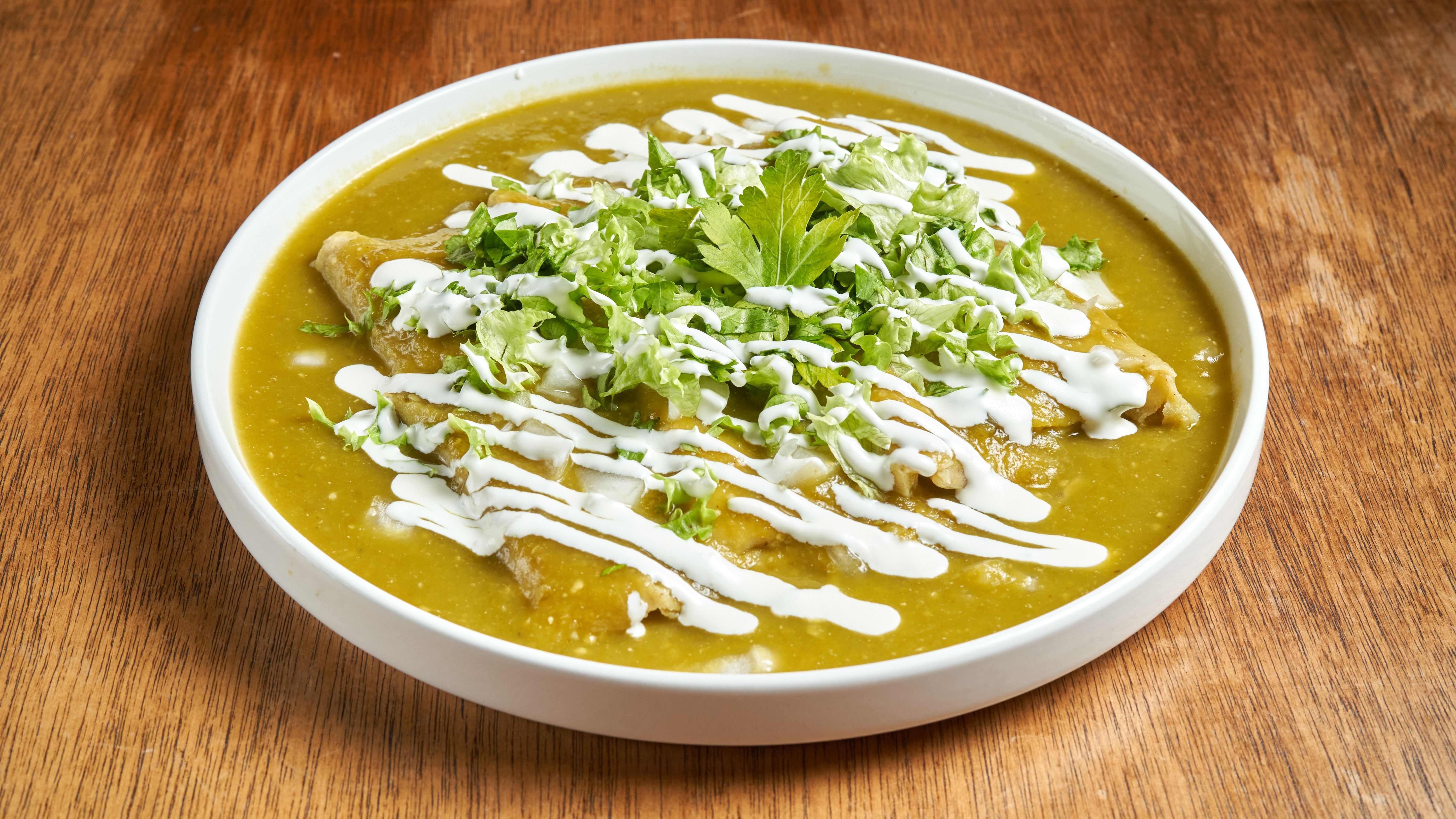Mouth-watering enchiladas topped with salsa verde, cream, and fresh herbs in a white dish.