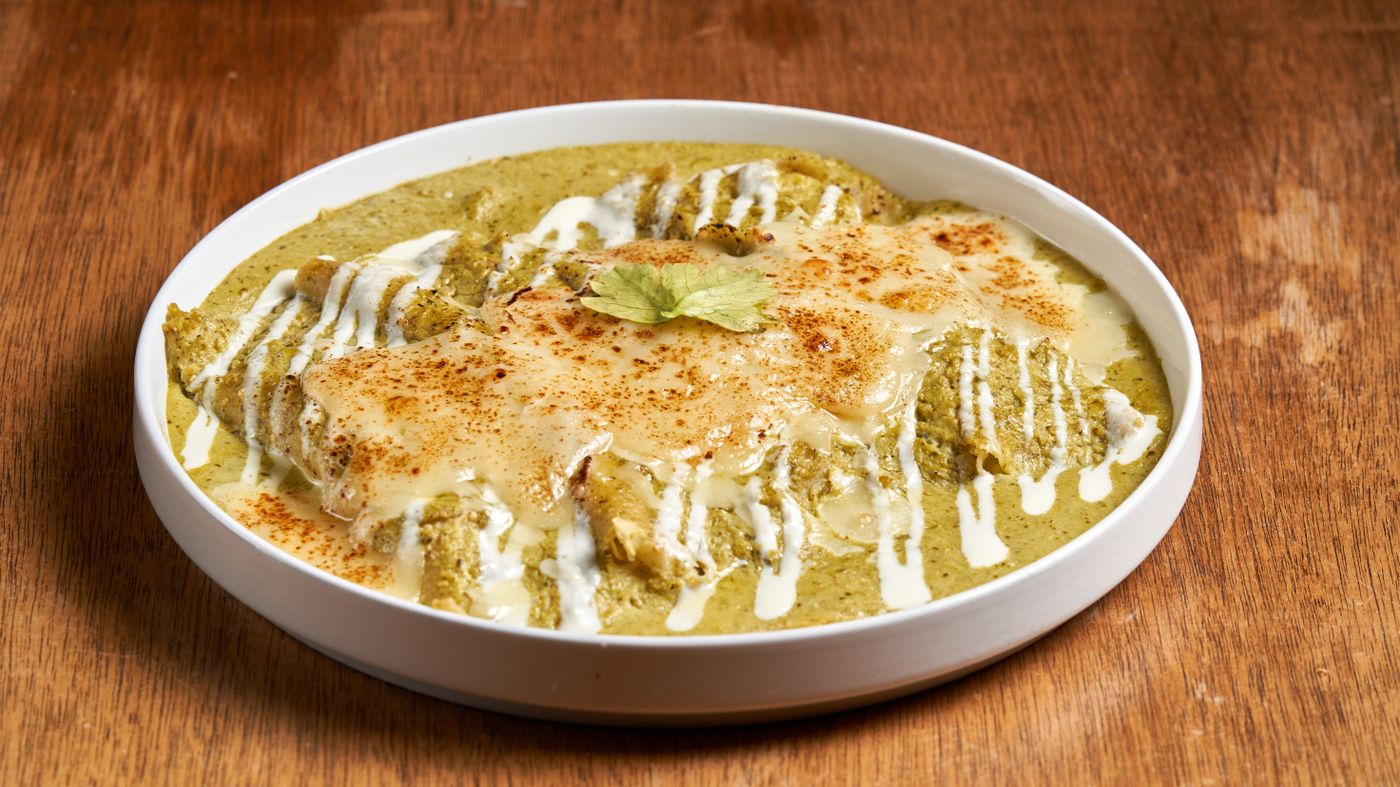 Tasty chilaquiles topped with cheese and crema served in a white bowl on a wooden table.