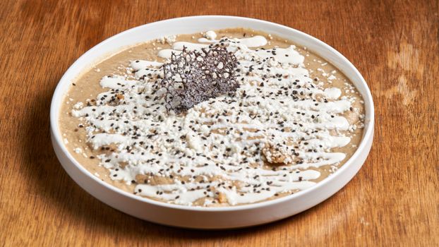 A top-down view of a gourmet dessert with creamy toppings and sesame seeds on a wooden table.