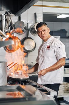 Chef in uniform expertly handles a flambé in a modern kitchen.