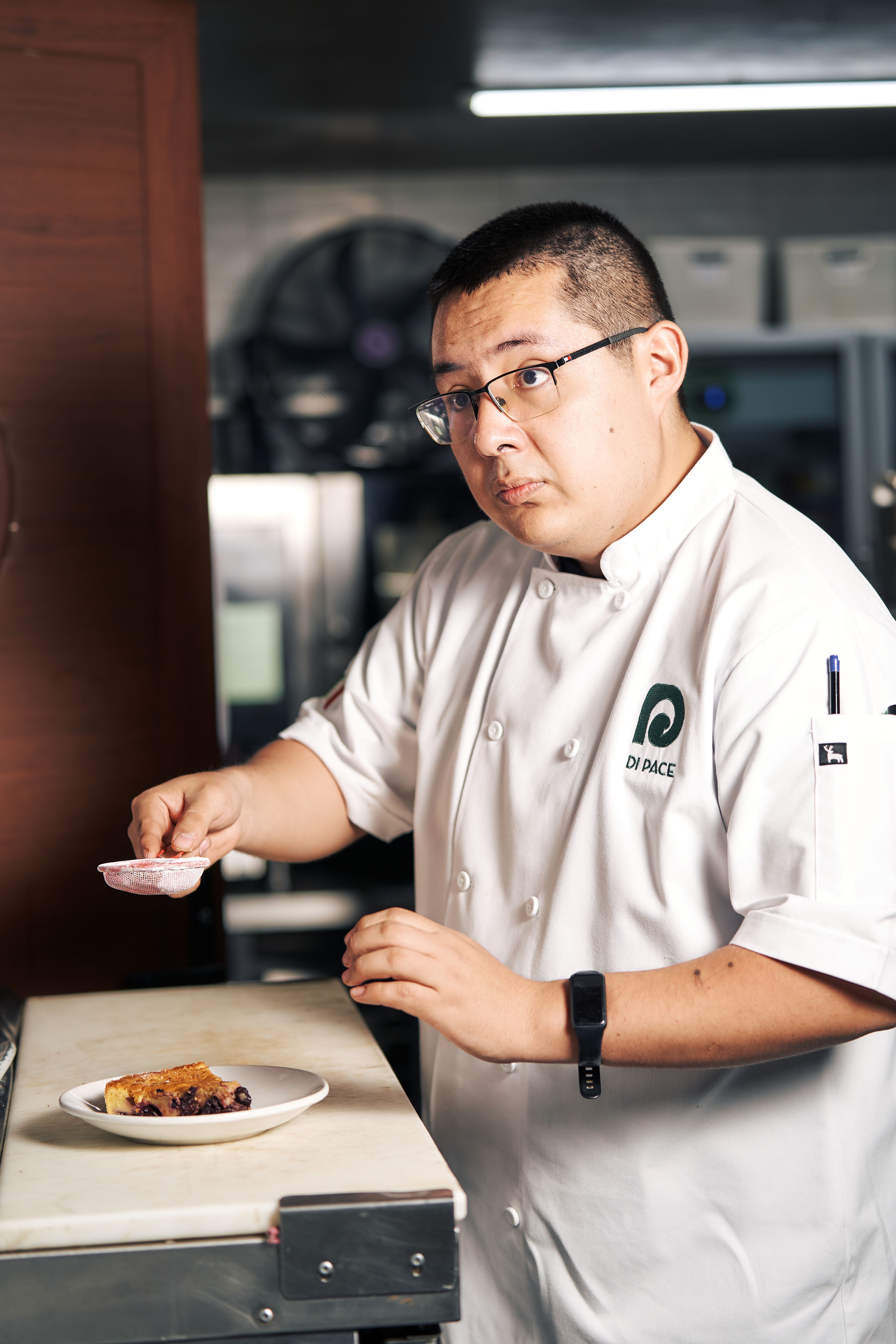 Chef in professional kitchen preparing a dessert with precision and focus.