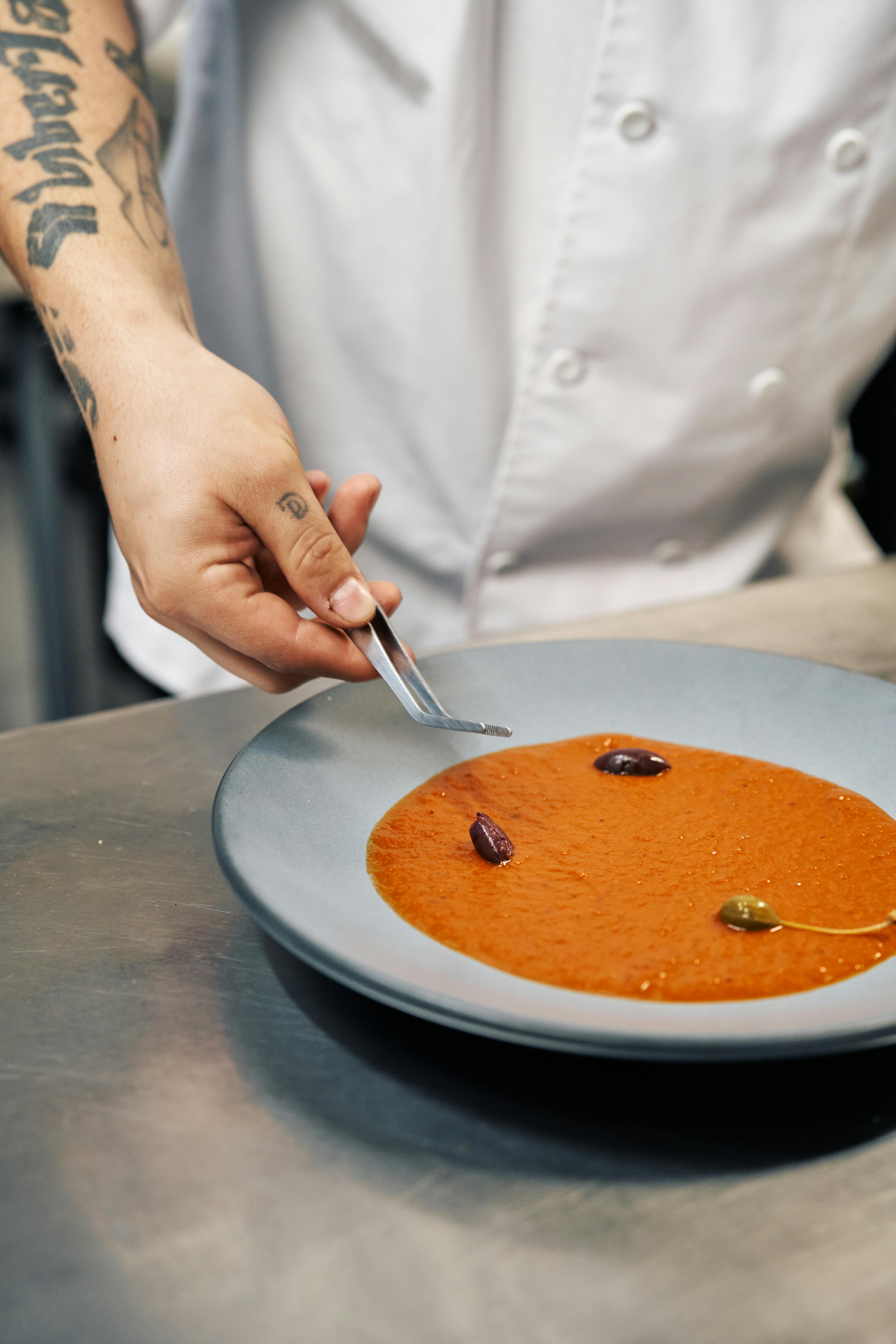 Chef adds final touches to a bowl of tomato soup with artistic garnishing.