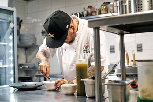 Free A chef wearing a cap skillfully prepares a dish in a modern kitchen setting. Stock Photo