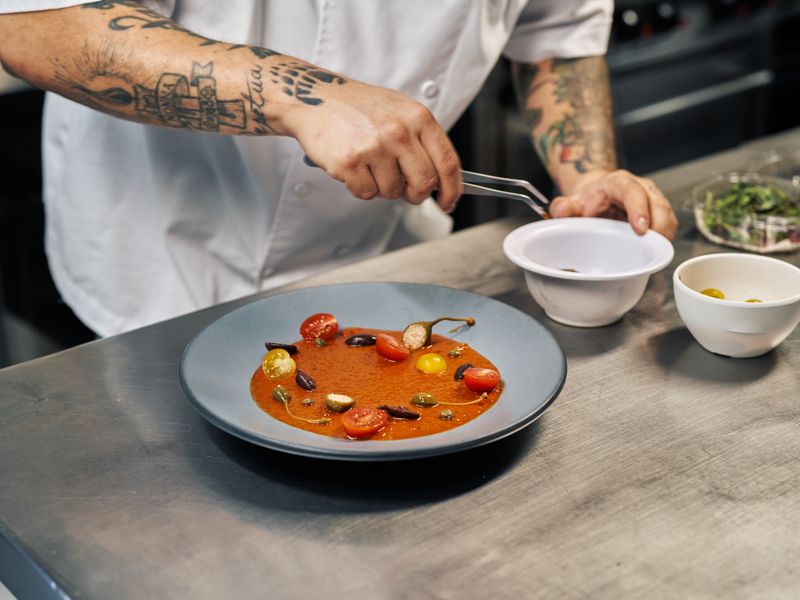 Chef dressant un gaspacho andalou rouge garni de tomates cerises, olives et herbes
