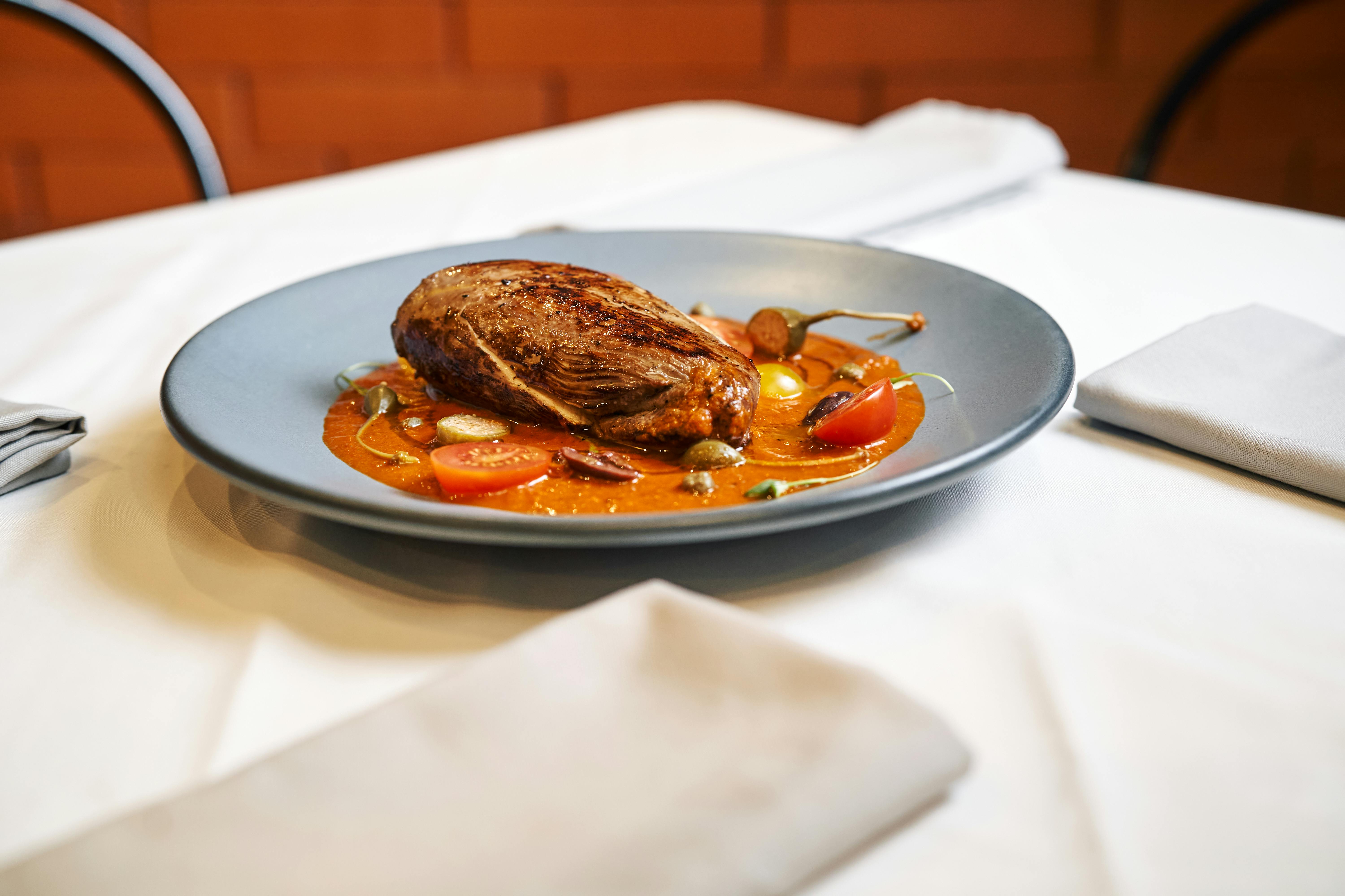 Elegant plated beef dish garnished with tomatoes on a sophisticated table setting.
