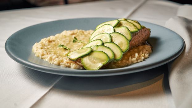 Delicious salmon topped with zucchini slices served on creamy risotto on a stylish plate.