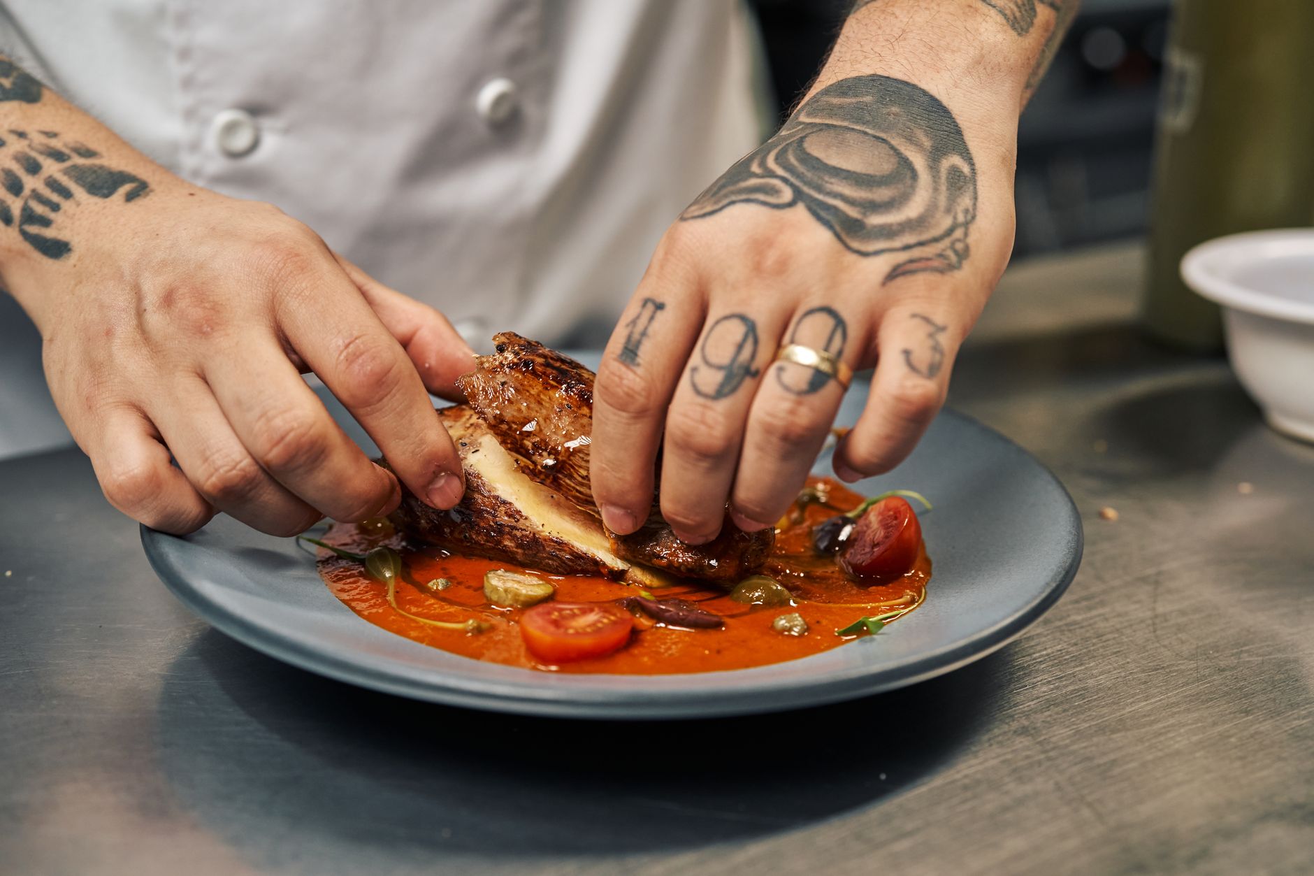 Close-up of a chef arranging a gourmet dish with chicken and tomatoes on a plate.