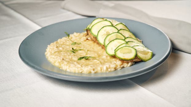 A plate of creamy risotto topped with fresh zucchini slices on a dining table.