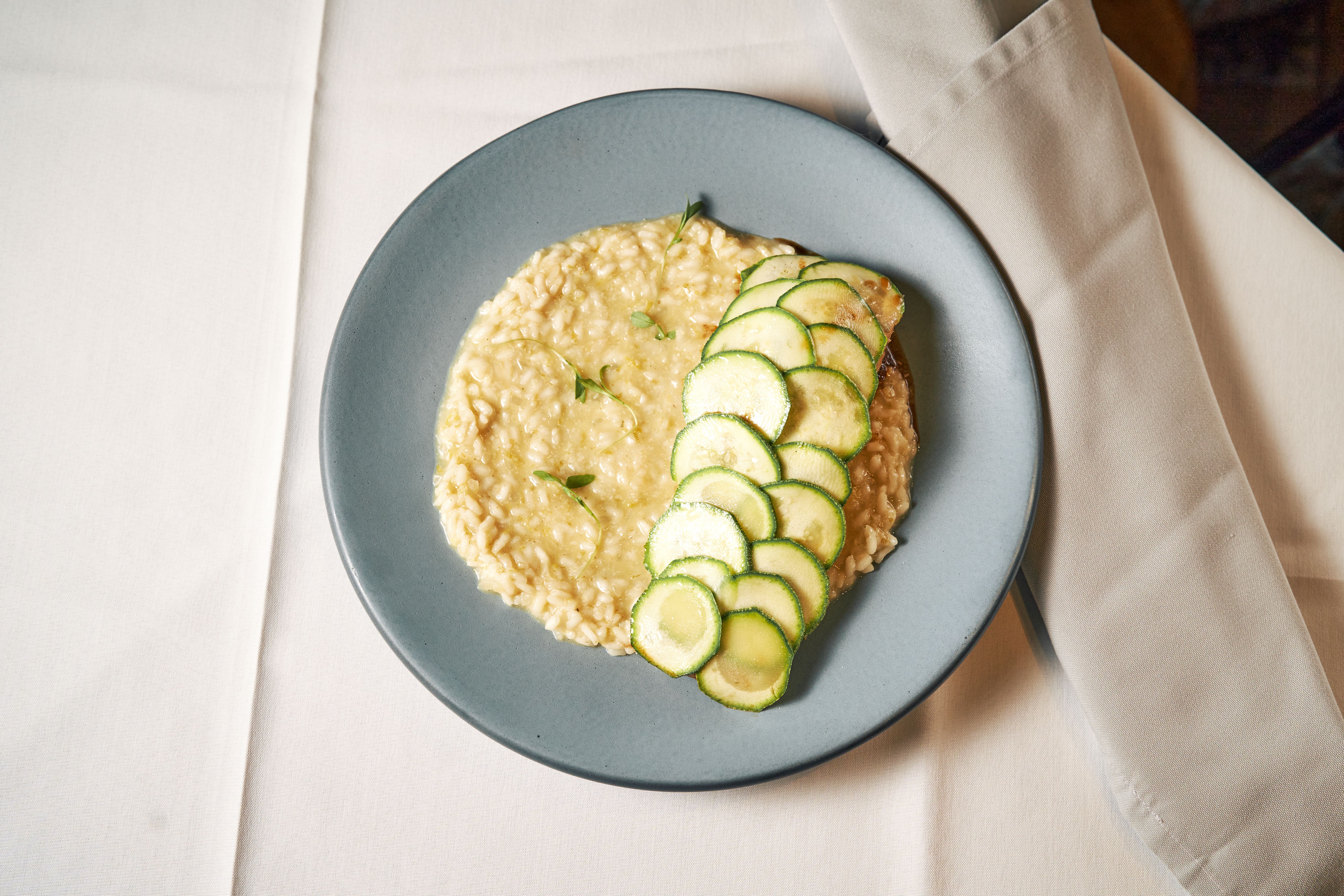 Creamy risotto served with fresh zucchini slices on a stylish table setting.