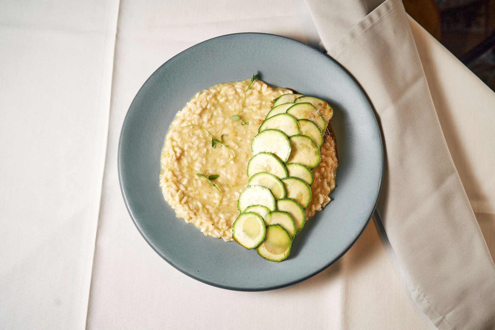 Creamy risotto served with fresh zucchini slices on a stylish table setting.