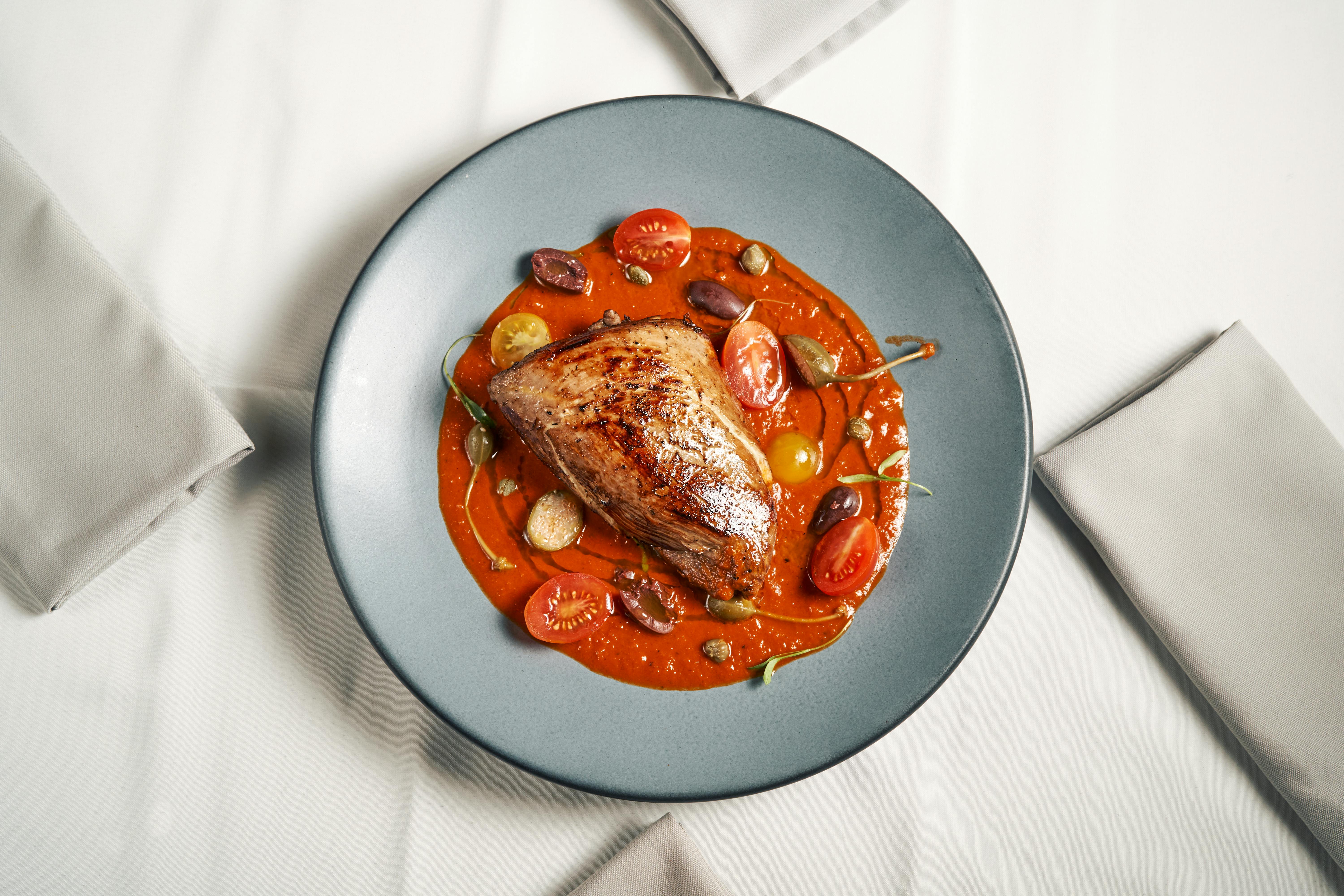 A delicately plated roast beef with tomato sauce, garnished with cherry tomatoes and olives.