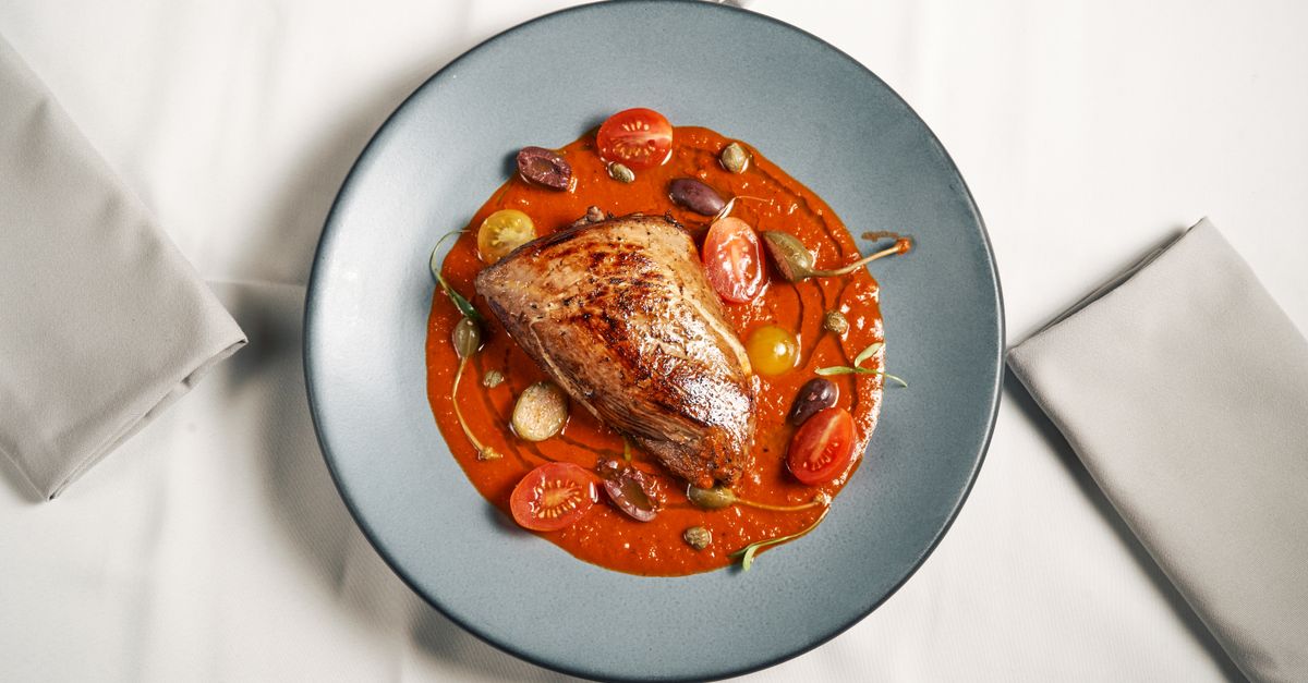 A delicately plated roast beef with tomato sauce, garnished with cherry tomatoes and olives.