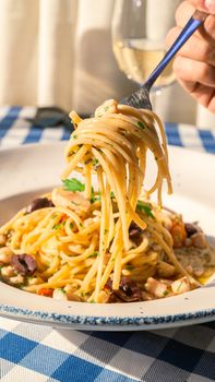 Close-up of a savory spaghetti aglio e olio dish with olives and parsley, served on a blue-checkered tablecloth.