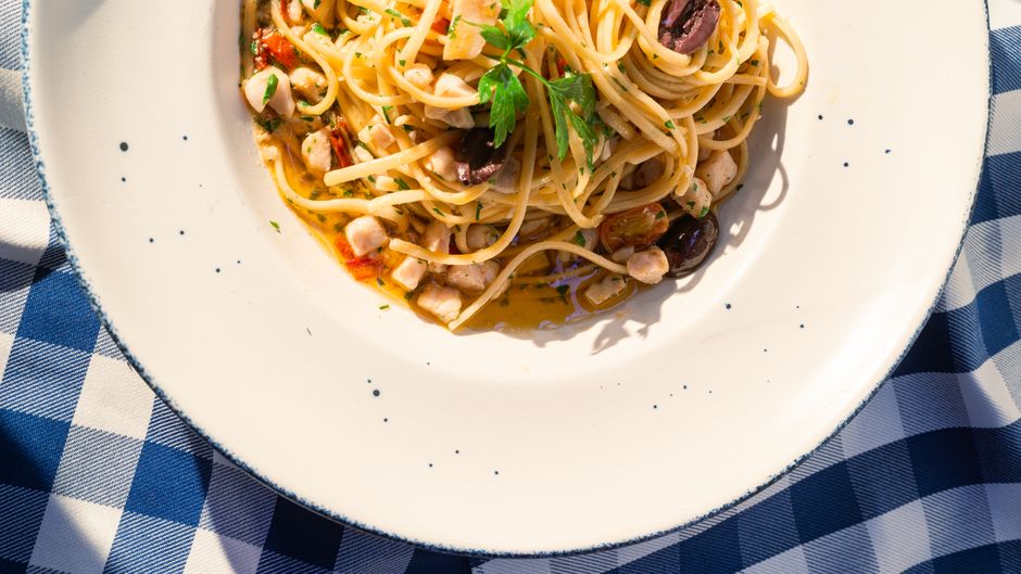Plate of spaghetti with seafood, olives on a checkered tablecloth.