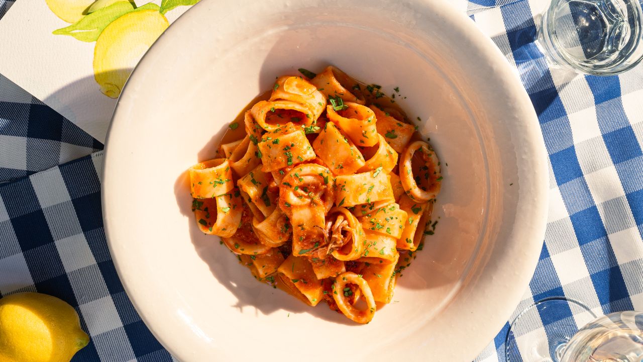 A sunlit outdoor table on the Amalfi Coast with a plate of calamari pasta and fresh lemons