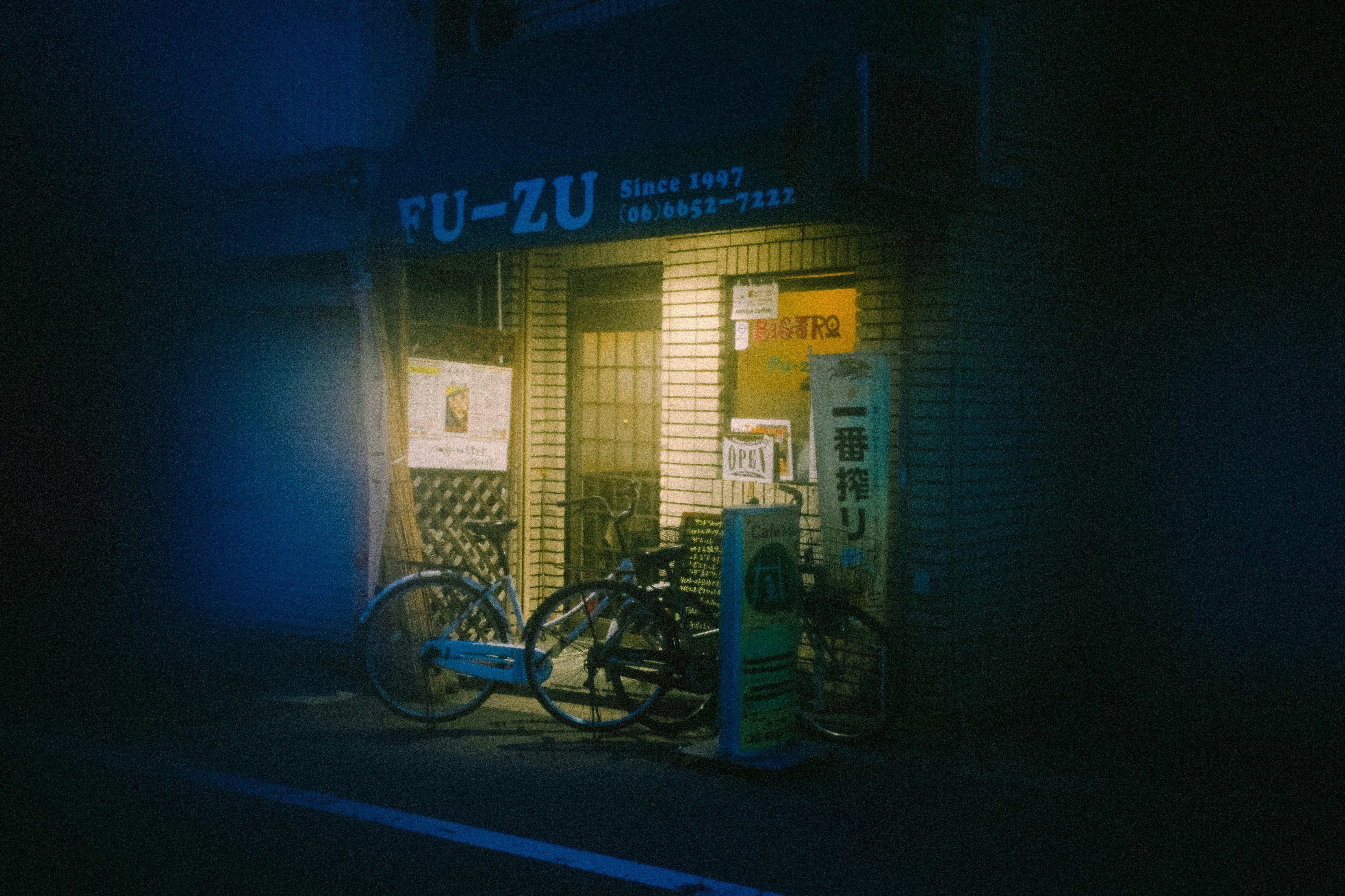Free Atmospheric night view of a small Japanese street corner shop with bicycles parked outside. Stock Photo