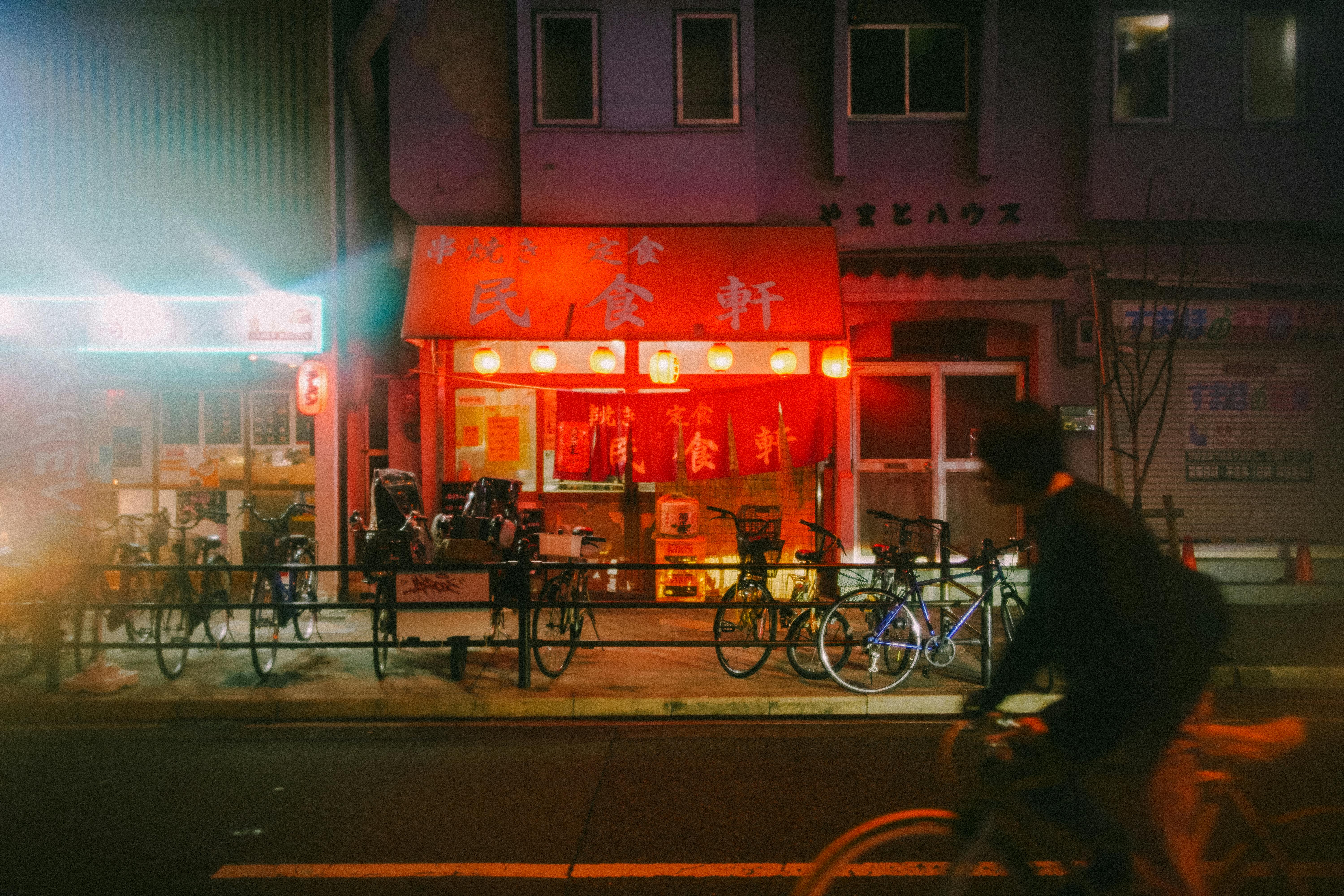 Bezpłatne Oszałamiający wieczorny widok japońskiej restauracji z przejeżdżającym rowerzystą. Zdjęcie z galerii