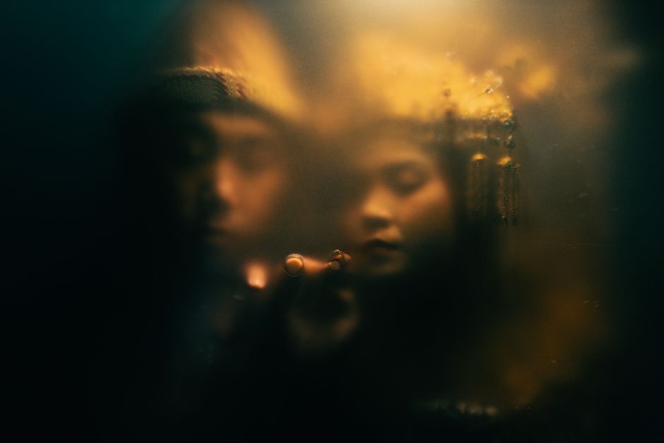 Two people create an enigmatic scene behind a steamy glass with warm lighting.
