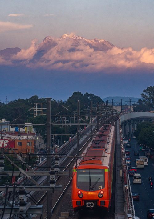 Free Orange metro train in Mexico City with a striking view of a snow-capped volcano in the distance. Stock Photo