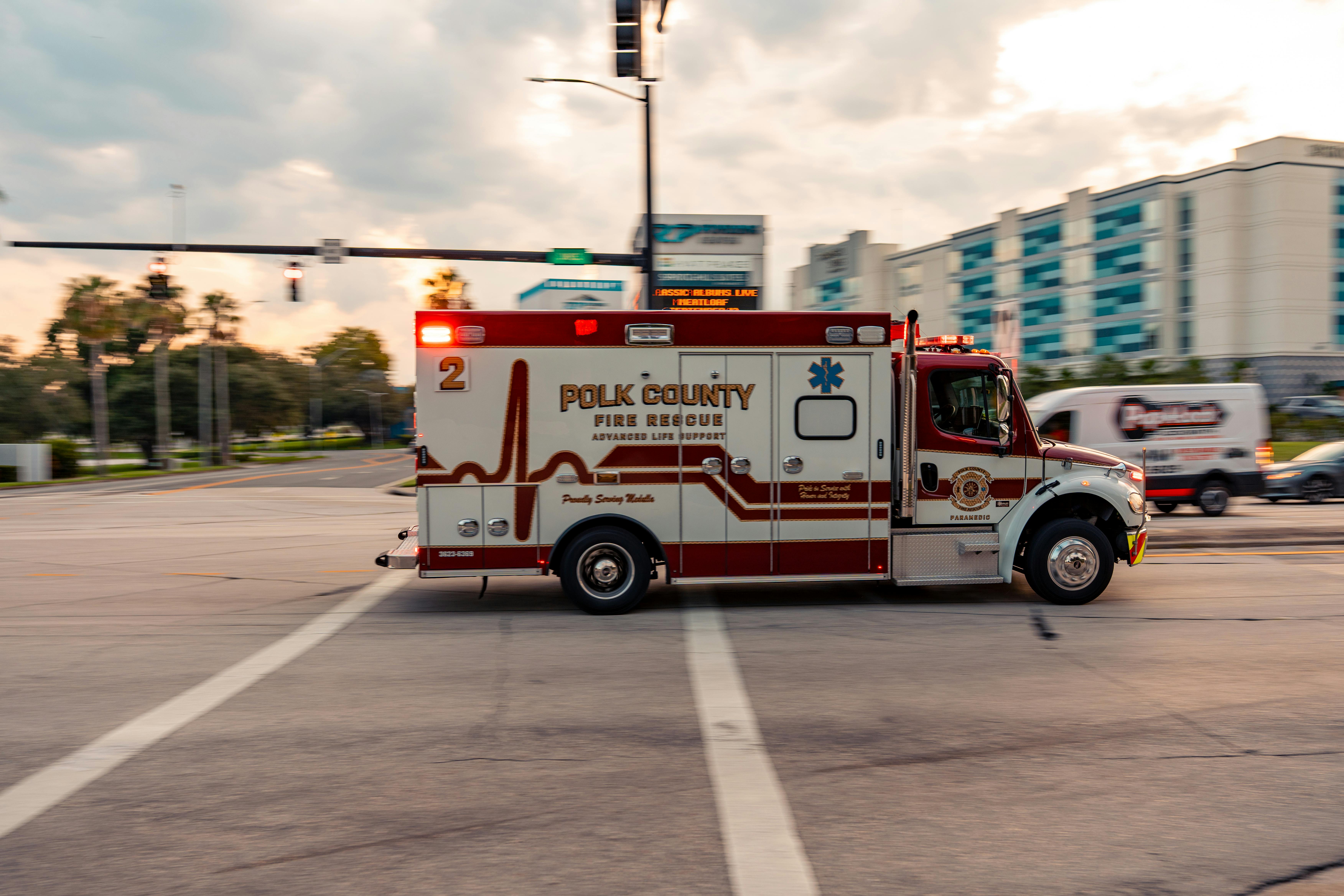 Polk County Fire Rescue Ambulance speeds through city intersection at sunset.