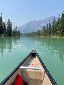 Scenic view from a canoe on a serene lake surrounded by evergreen trees and distant mountains.