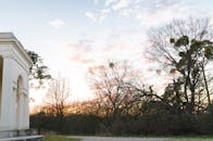 黎明时分，莱德尼斯-瓦尔蒂斯公园内，美丽的历史建筑被树木环绕，天空五彩缤纷