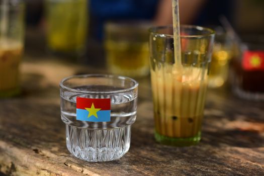 Close-up of glass drinks with Vietnamese flag sticker on a rustic wooden table. Sunlight creates a warm vibe.
