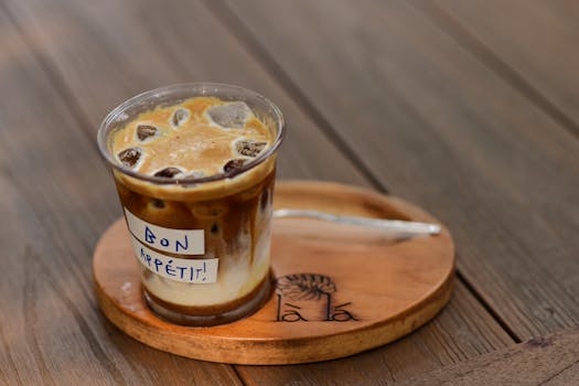 Iced coffee in a clear cup with 'Bon Appétit' label, served on a wooden tray.