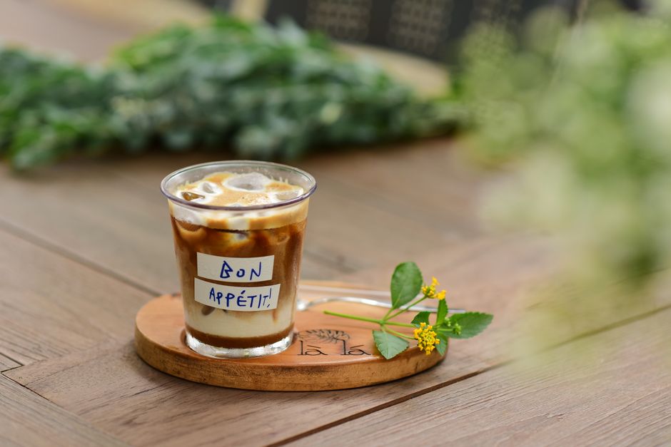 A cup of coffee with foam served on a wooden tray displaying the note 'Bon Appétit!'