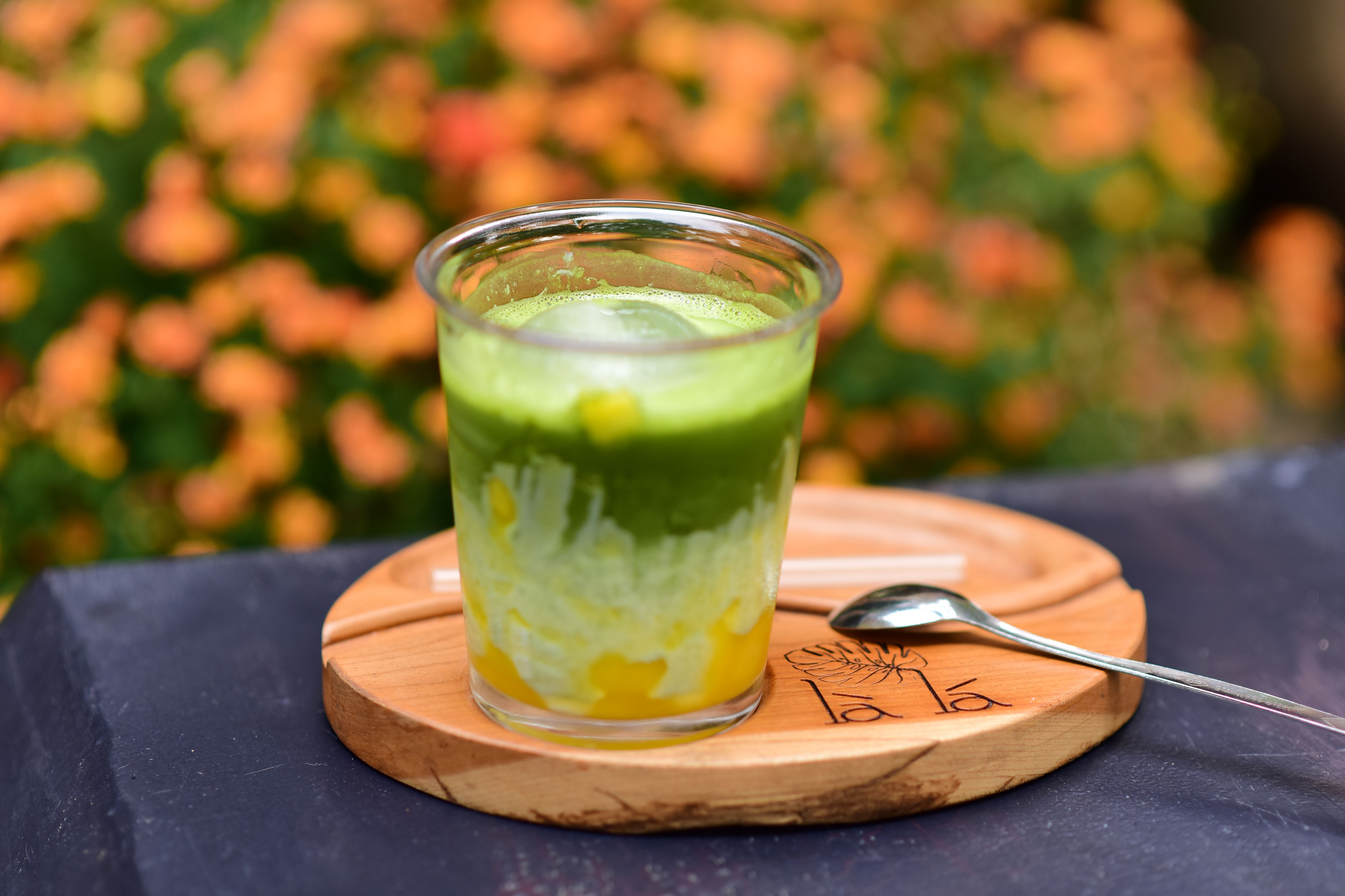 A vibrant glass of iced matcha green tea with orange flowers in the background, ideal for outdoor dining settings.