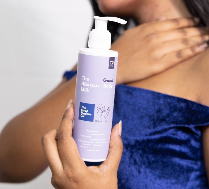 A close-up of The Hibiscus Milk skincare lotion being held by a woman, emphasizing soft skin care.