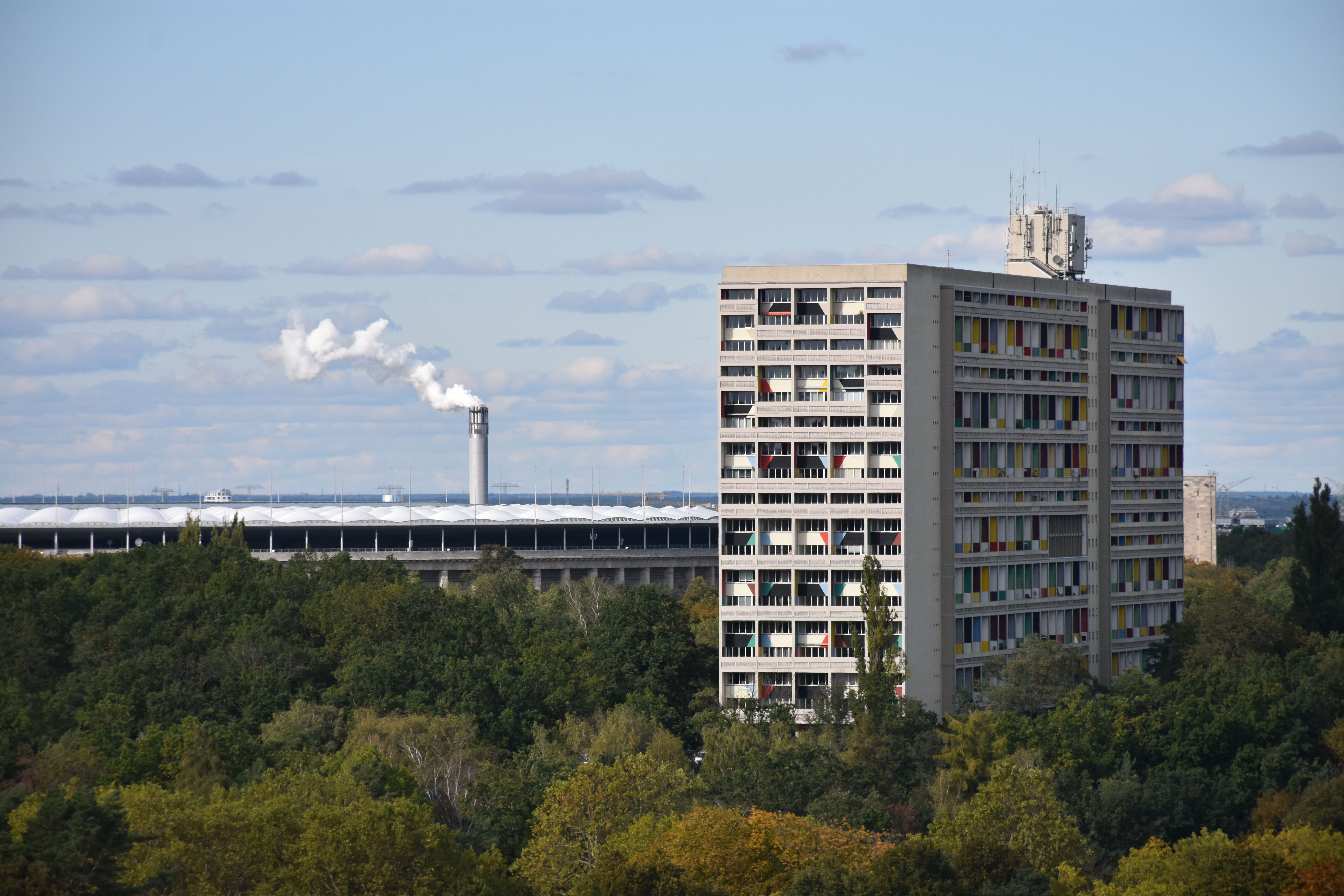 High-rise building beside Berlin's Olympic Stadium surrounded by greenery under blue skies. — Trójmiasto
