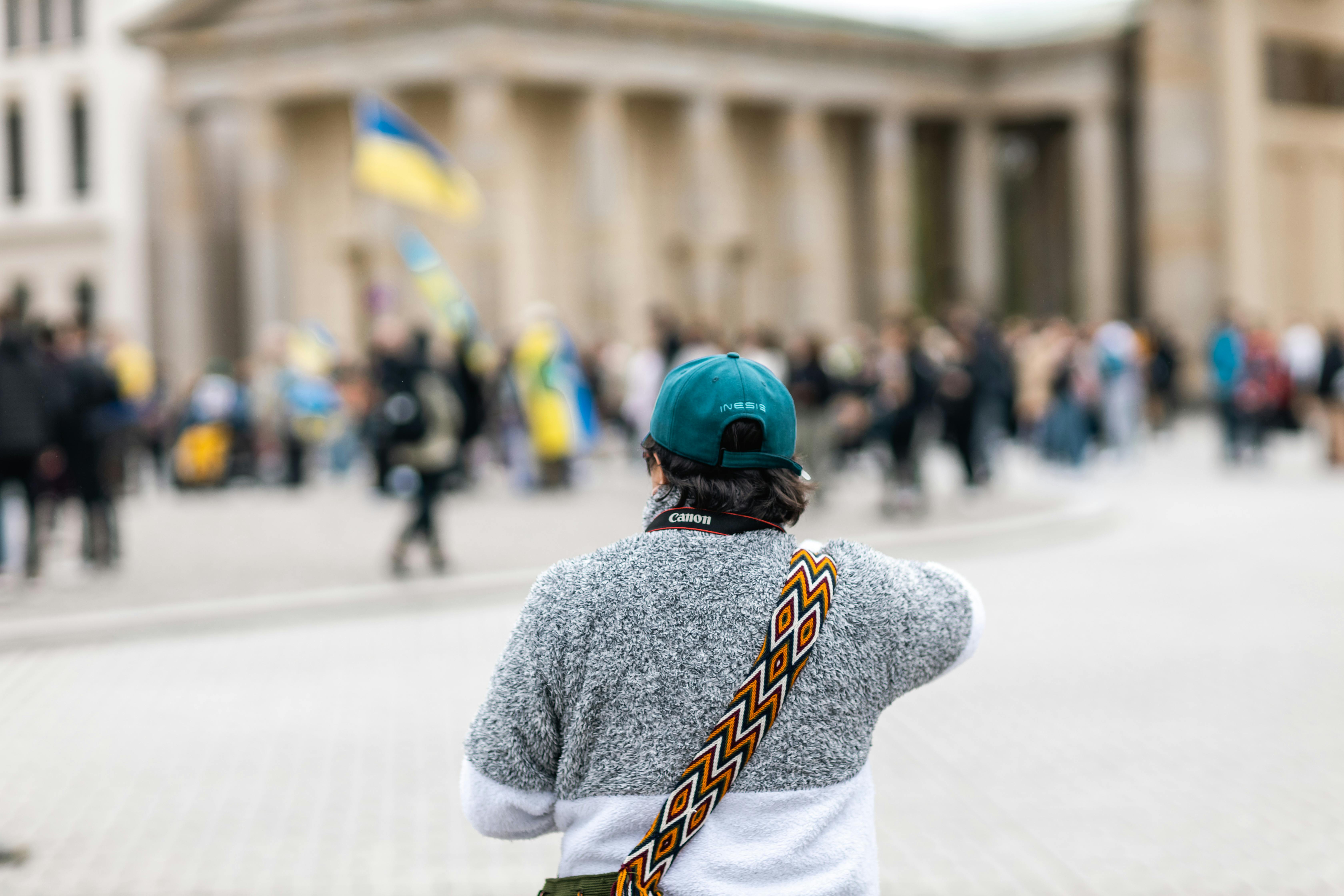 A photographer with a camera explores an urban square bustling with people.