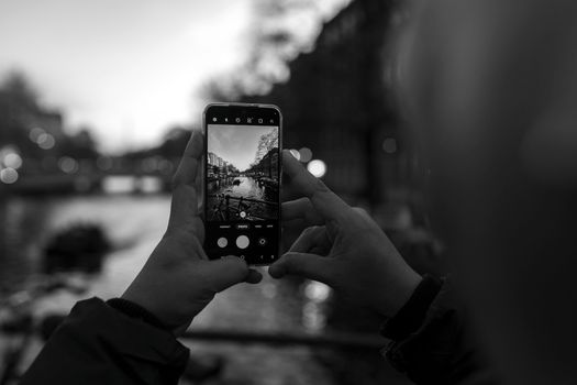 A person captures a canal view on a smartphone in Amsterdam during twilight.