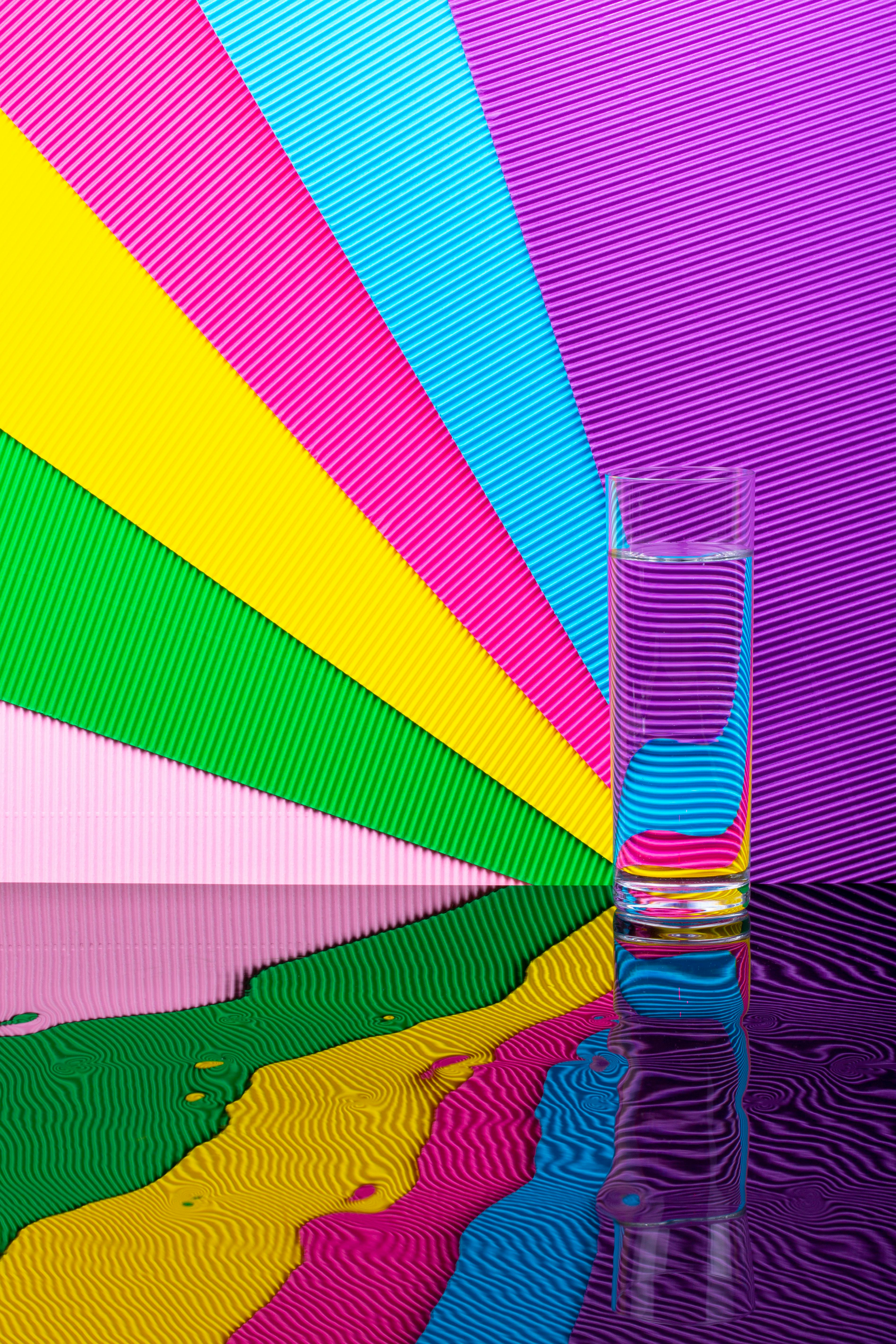 Gratis Un bicchiere d'acqua è posto su uno sfondo vivace e colorato con riflessi, che mette in mostra l'arte moderna e i concetti astratti. Foto a disposizione