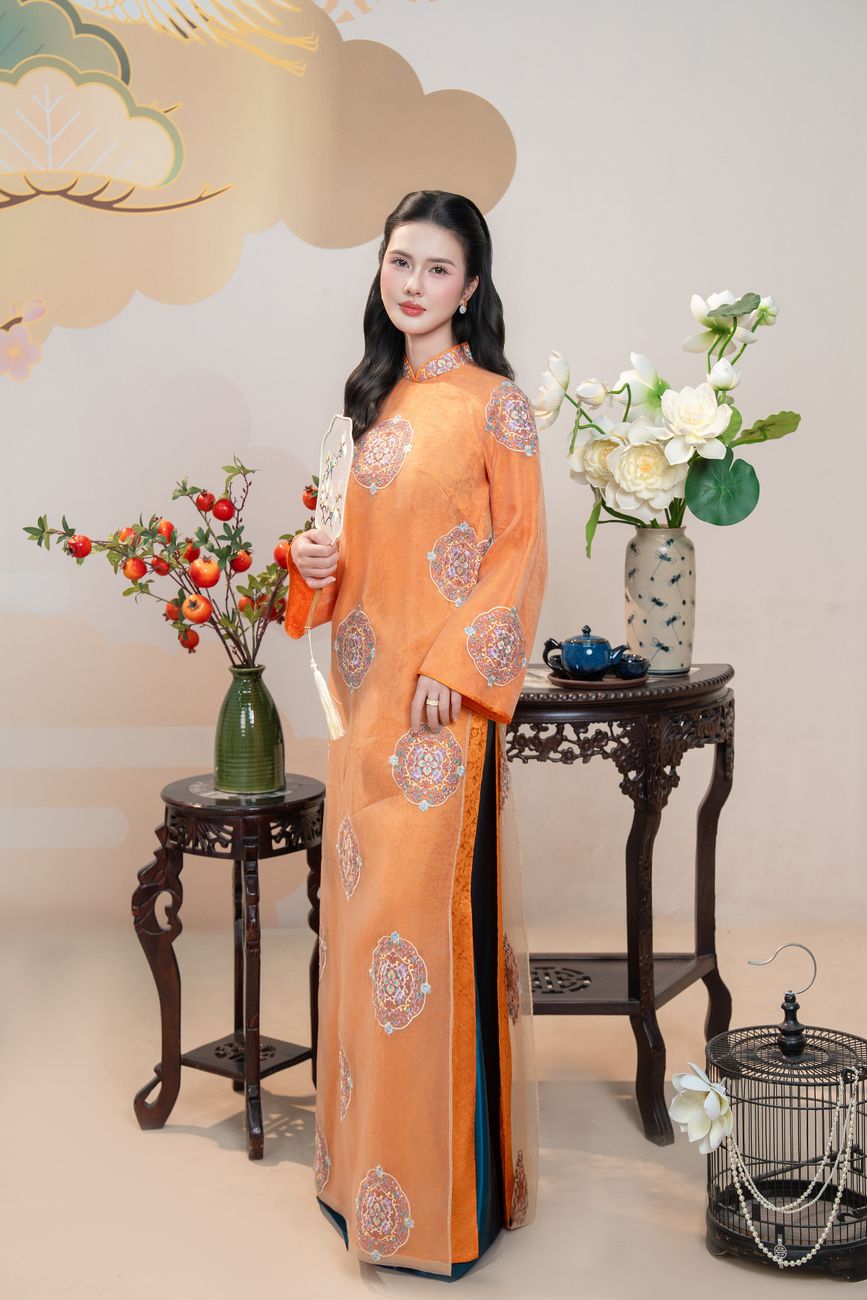 Woman in orange Áo Dài with floral decor and Vietnamese table.