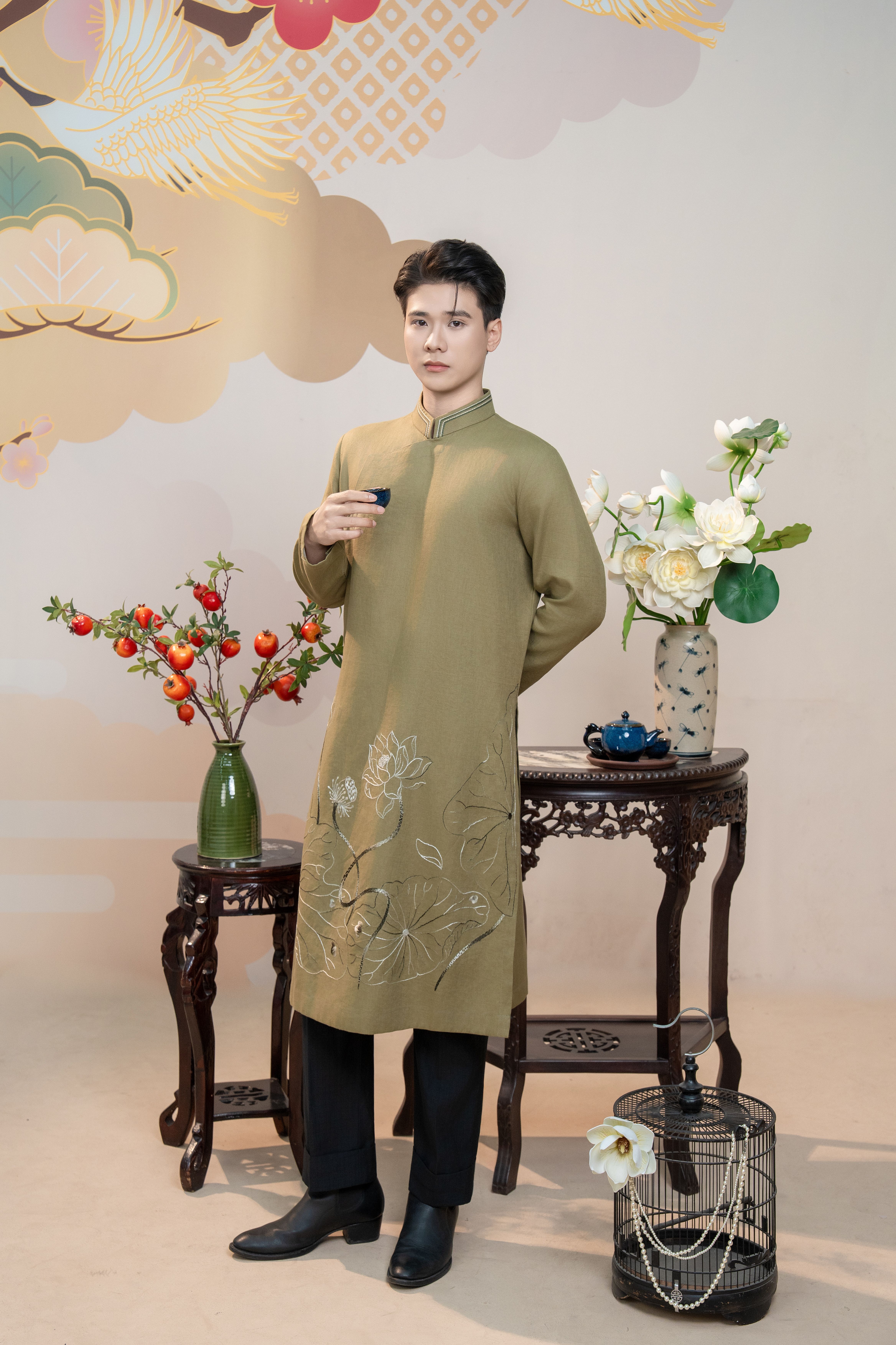 Man wearing traditional Asian outfit standing by an ornate table indoors.