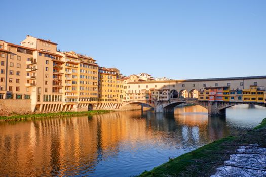 Beautiful sunset view of Ponte Vecchio reflected on the Arno River in Florence, Italy.