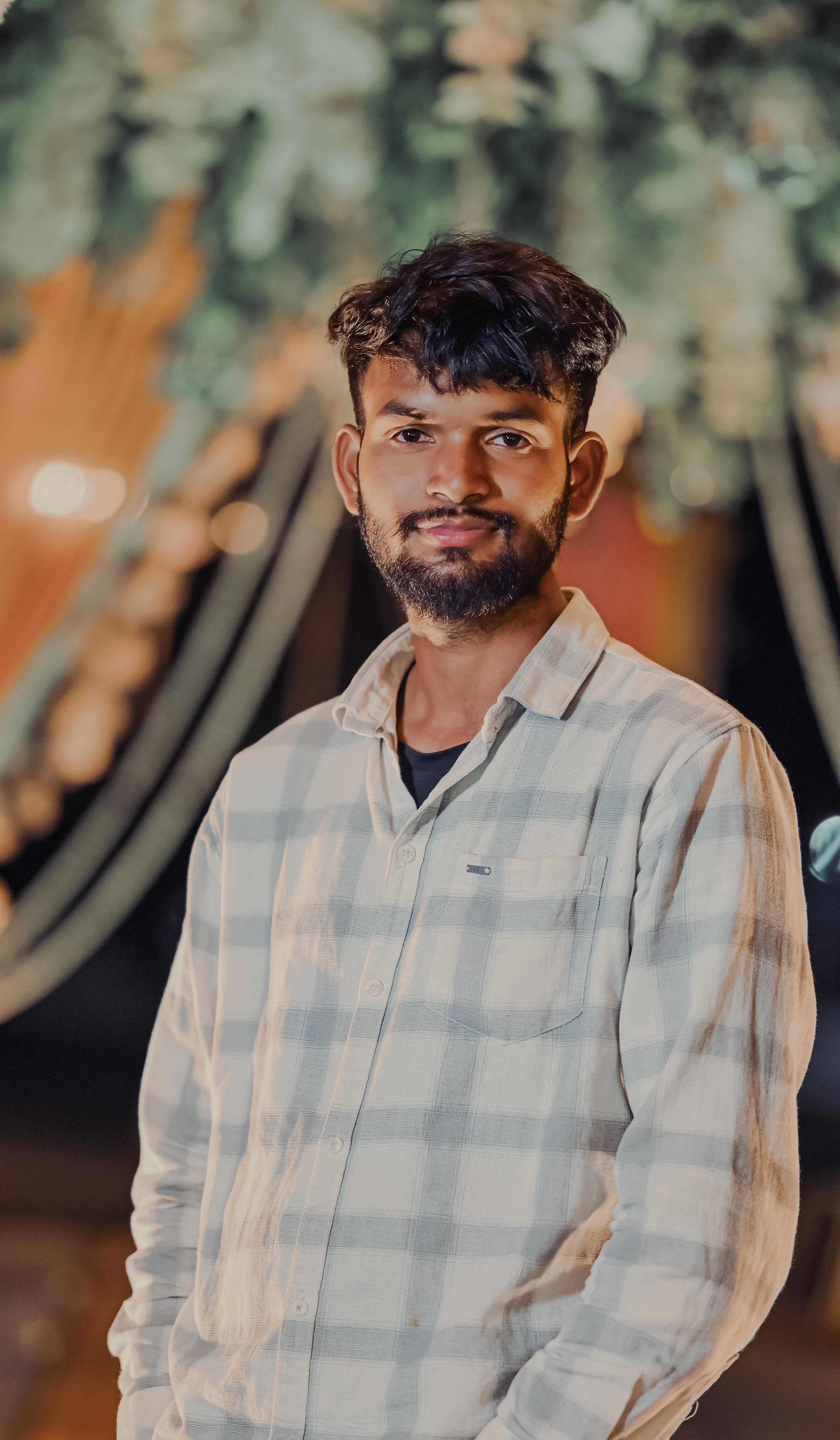 Smiling man in checkered shirt at an outdoor evening event with festive background.