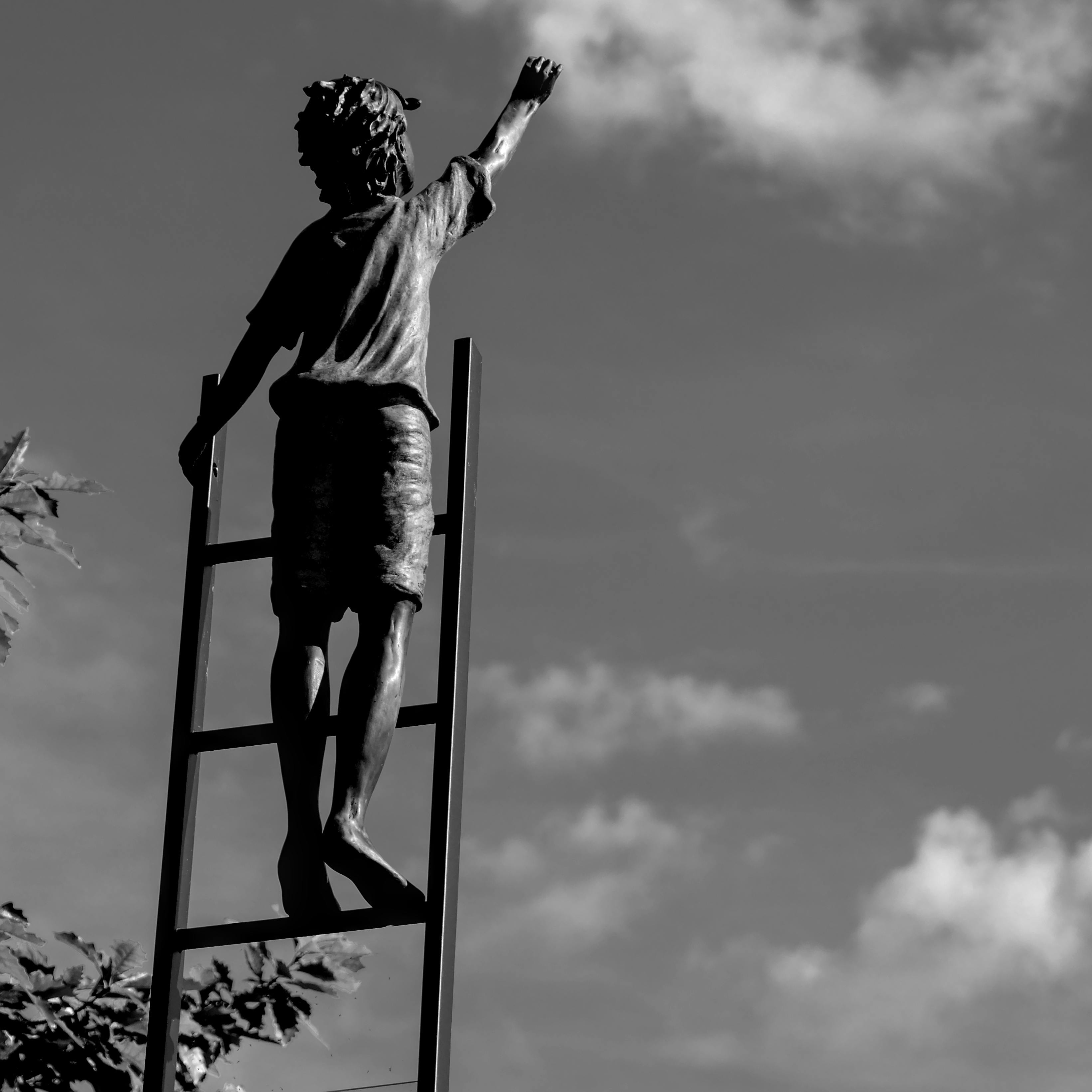 бесплатная Черно-белая скульптура, изображающая ребенка, тянущегося вверх, стоя на лестнице под открытым небом. Стоковое фото