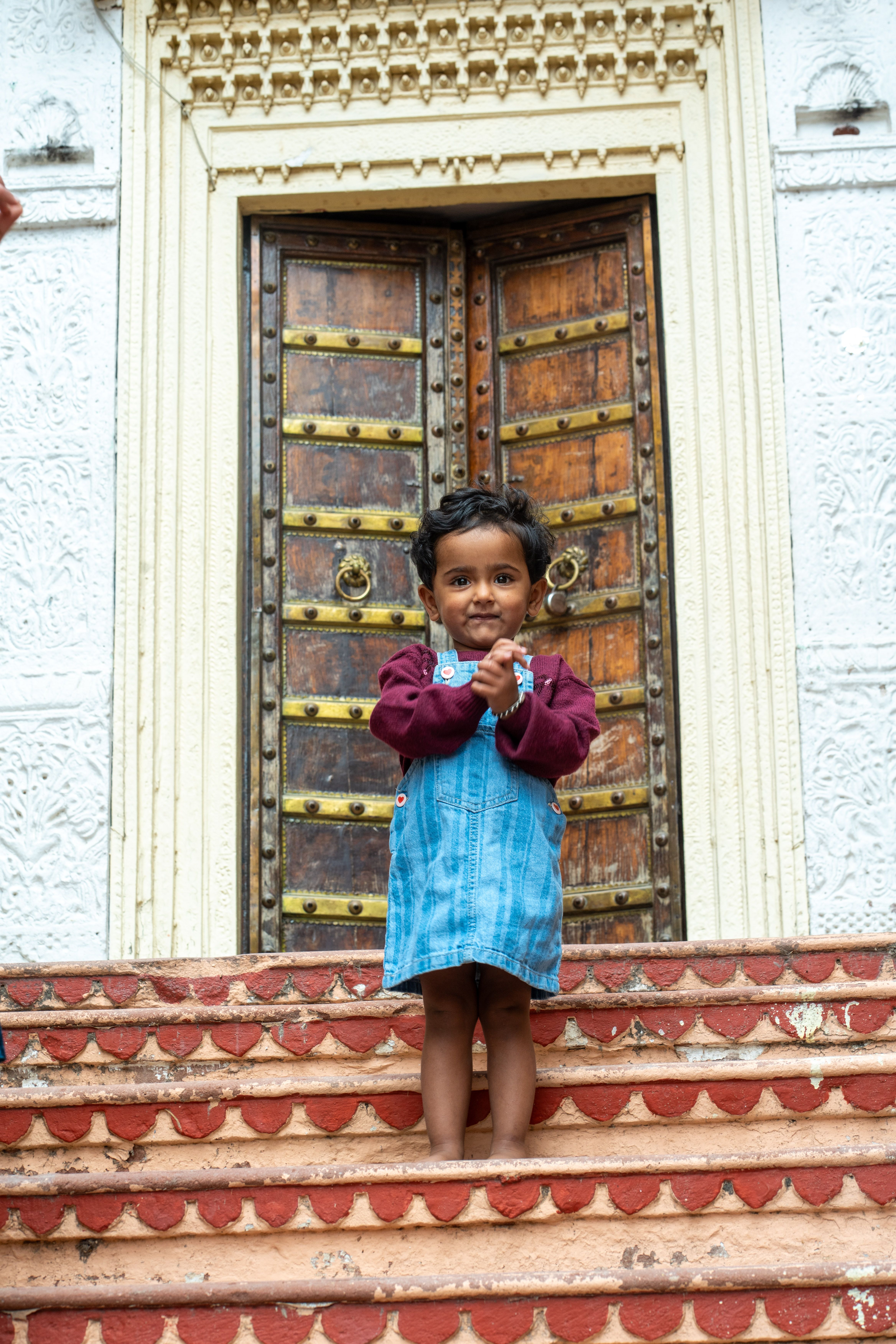 Smiling Child Posing in Front of Ornate Wooden Door · Free Stock Photo