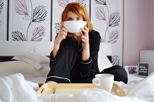 Free Woman in Pajamas Sitting on the Bed Holding a Bowl Stock Photo