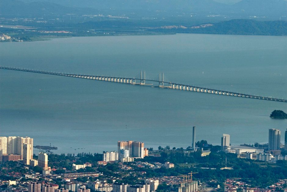 Aerial view of the Penang Bridge stretching above the calm waters with Penang city in the foreground.