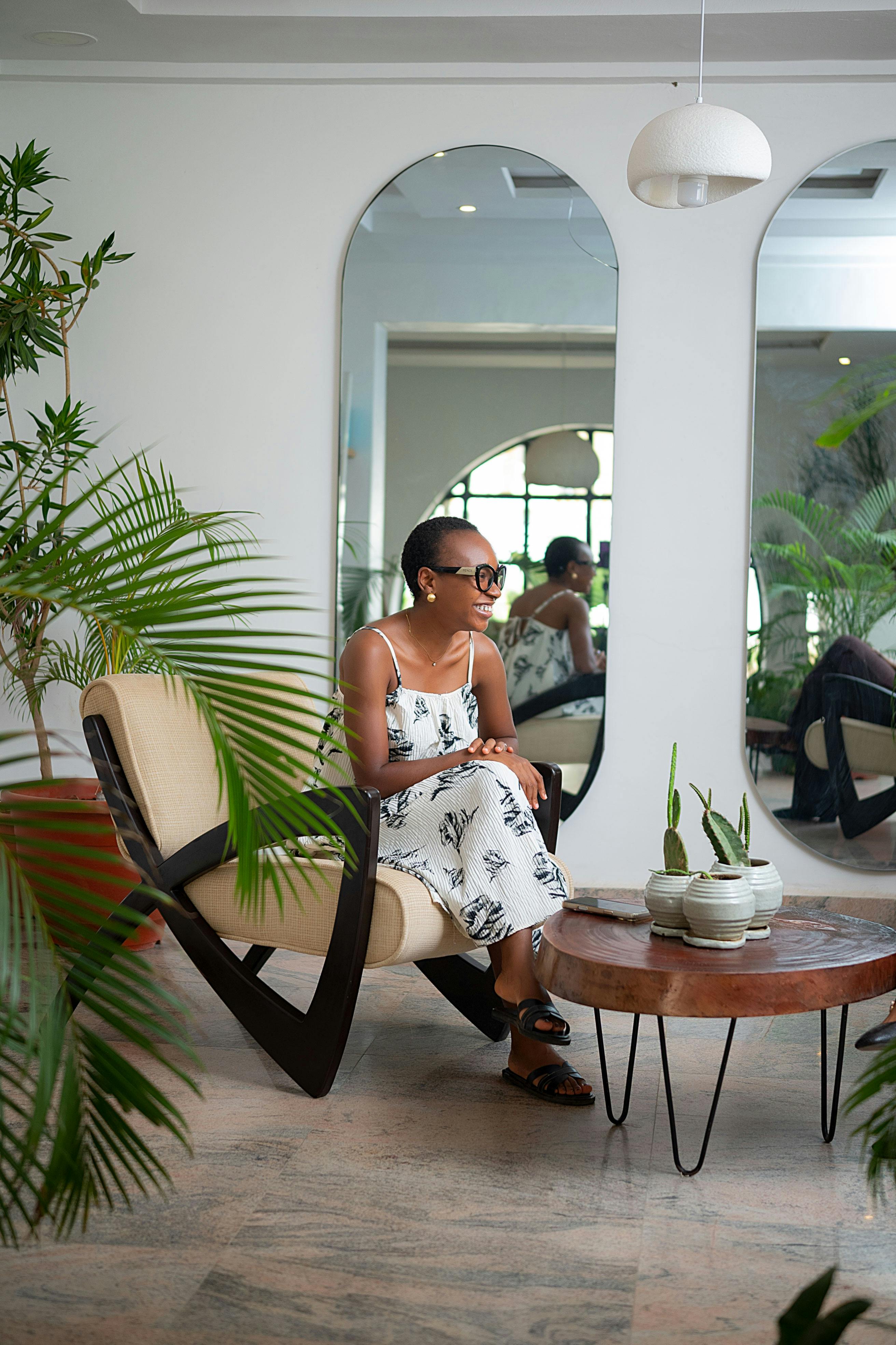 бесплатная Модная женщина в платье с узором отдыхает в стильном интерьере, окруженном пышной зеленью и современным декором. Стоковое фото