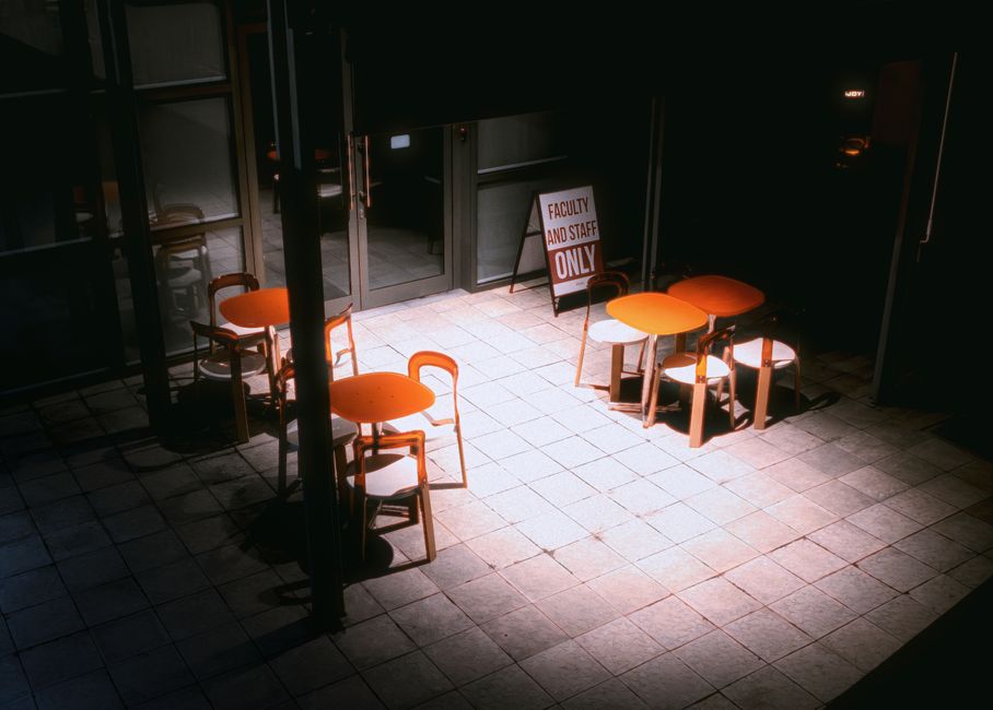 Moody nighttime shot of empty patio tables and chairs with a restricted access sign.