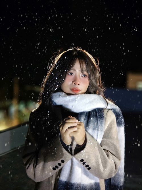 Free A young woman wearing a coat and scarf enjoying a snowy night in Vietnam. Stock Photo