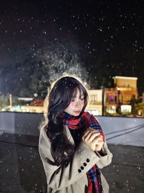 Free A young woman stands under falling snow at night, wrapped in a warm scarf and coat. Stock Photo