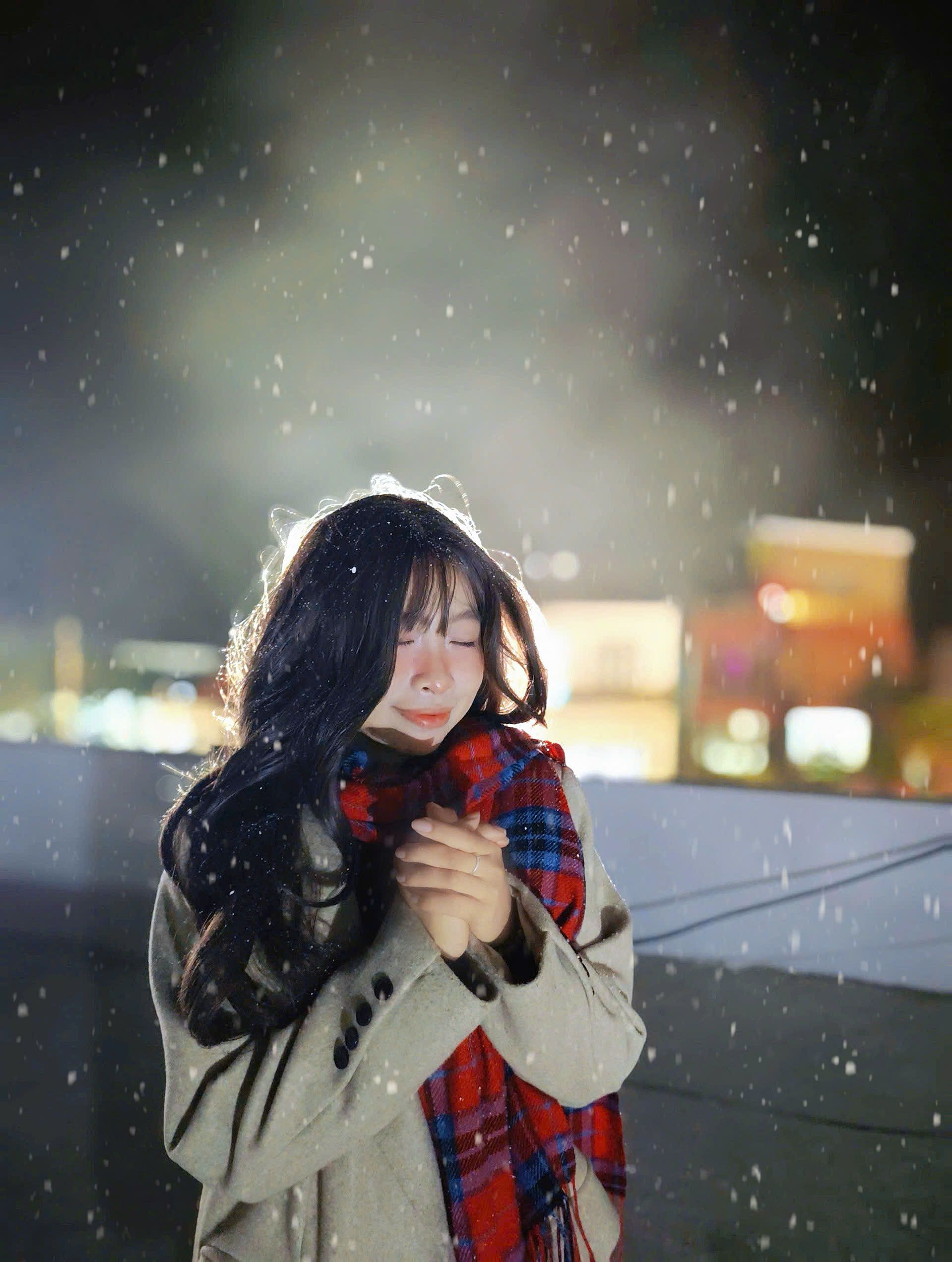 Captivating image of a woman standing in snowfall at night, experiencing winter joy in Vietnam.
